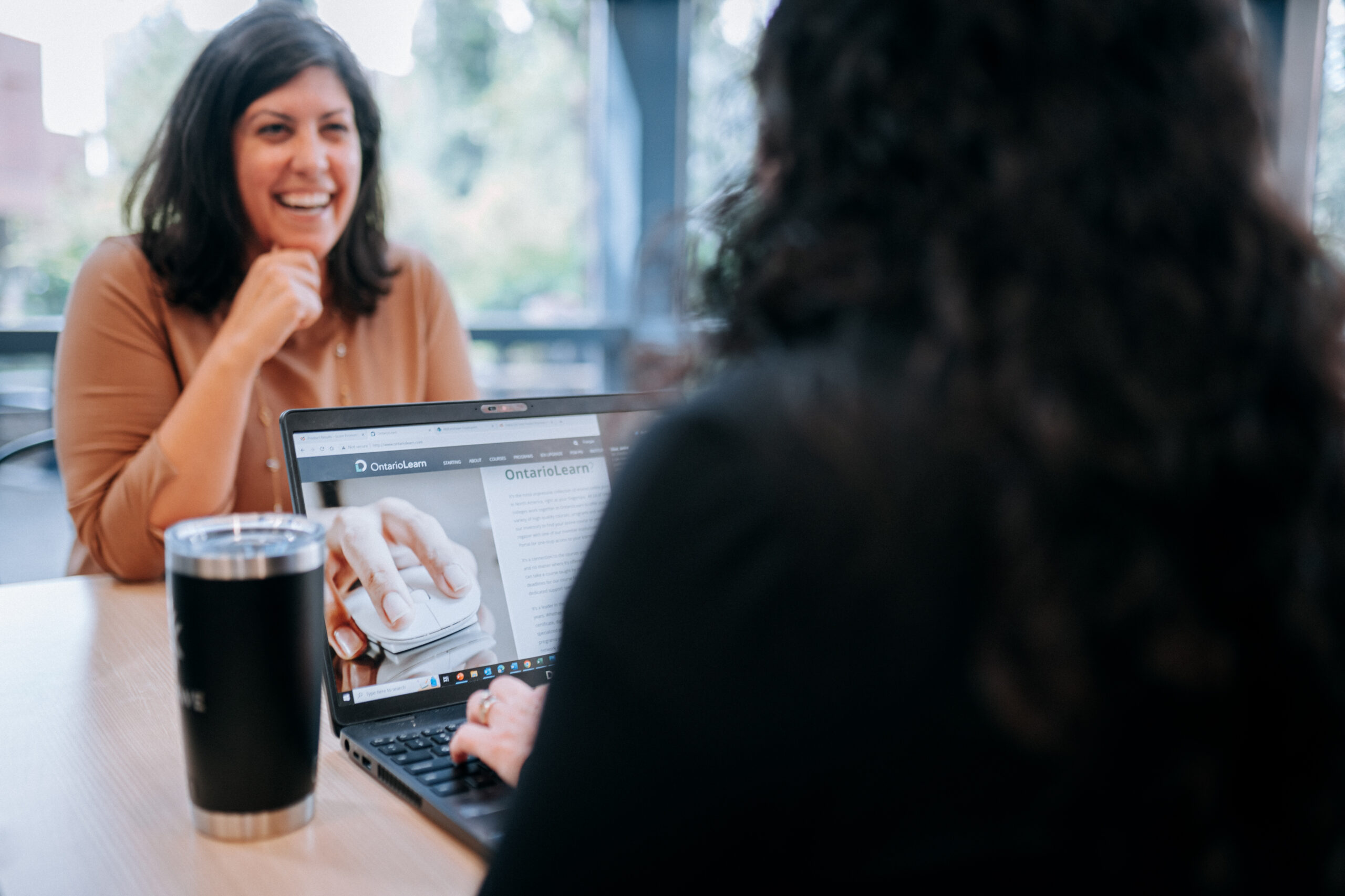 Two women discussing their college options at a table with laptop computers to look data up on. 